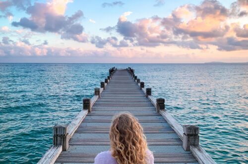 Person sitting peacefully on a dock overlooking the ocean at sunset