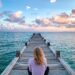 Person sitting peacefully on a dock overlooking the ocean at sunset
