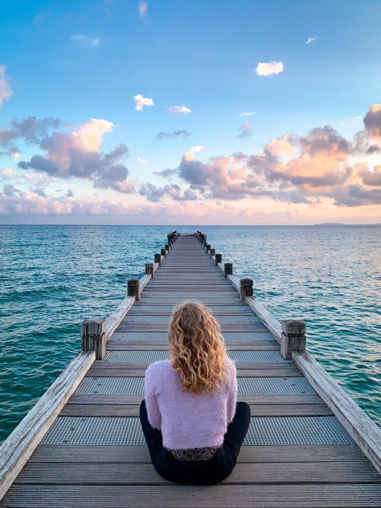 Person sitting peacefully on a dock overlooking the ocean at sunset