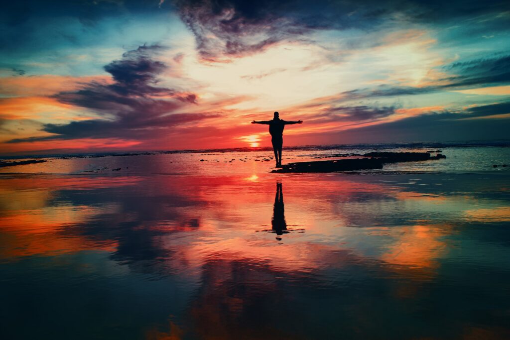 Person standing in shallow ocean water at sunrise, reflecting on healing, trust, and new beginnings.