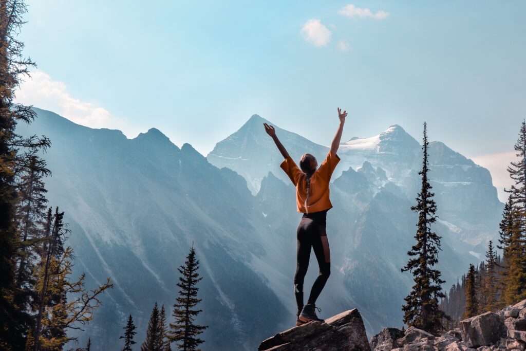 A person standing on a mountain with their arms raised, symbolizing quiet success, personal growth, resilience, and celebrating meaningful victories.