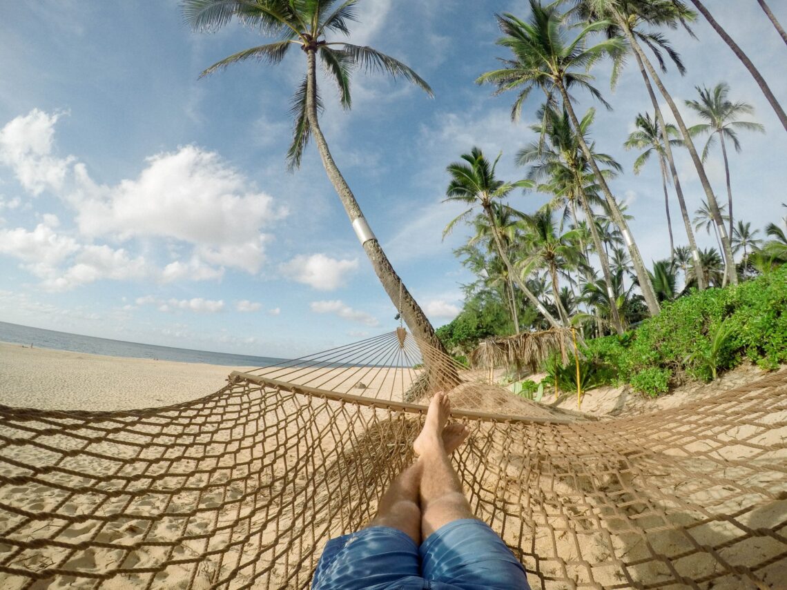 A hammock hanging between palm trees on a peaceful beach, symbolizing rest, recovery, slowing down, and personal growth.