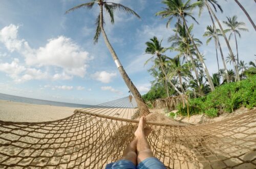 A hammock hanging between palm trees on a peaceful beach, symbolizing rest, recovery, slowing down, and personal growth.