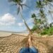 A hammock hanging between palm trees on a peaceful beach, symbolizing rest, recovery, slowing down, and personal growth.