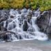 Waterfall flowing over rocks surrounded by green foliage